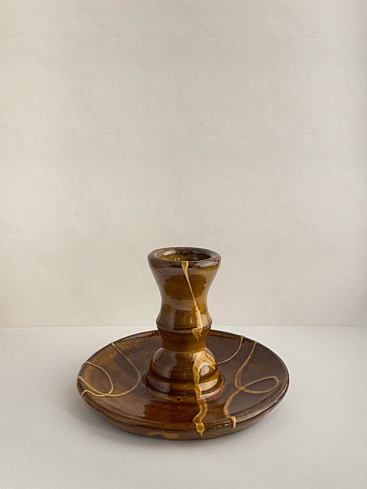Brown and gold handmade ceramic candle holder with decorative patterns on a neutral background - front view.