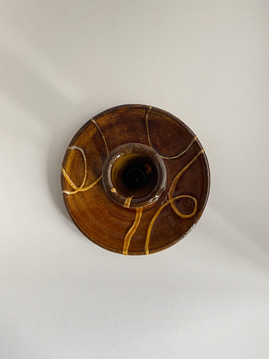 Brown and gold handmade ceramic candle holder with decorative patterns on a neutral background - top view.