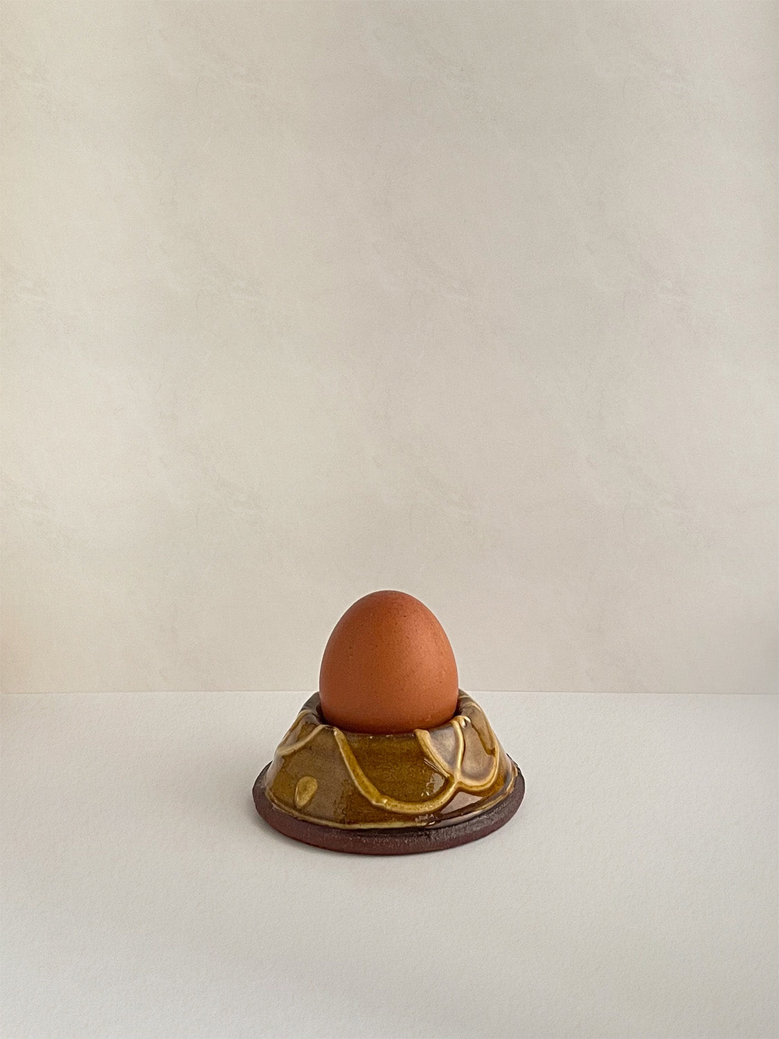 Brown and gold handmade ceramic egg cup with an egg on a neutral background.