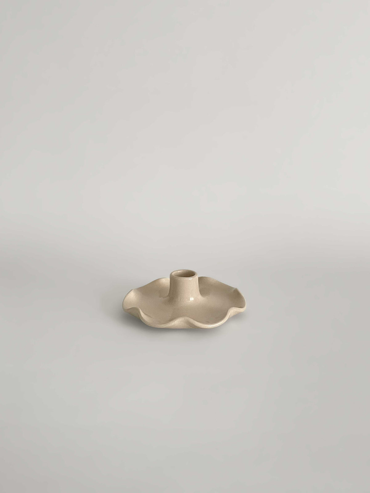 A handmade ceramic candle holder with a softly frilled base and a central cylindrical stem, on a neutral background.