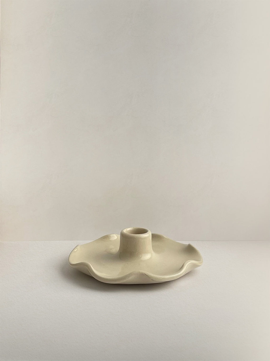 A handmade ceramic candle holder with a softly frilled base and a central cylindrical stem, on a neutral background.