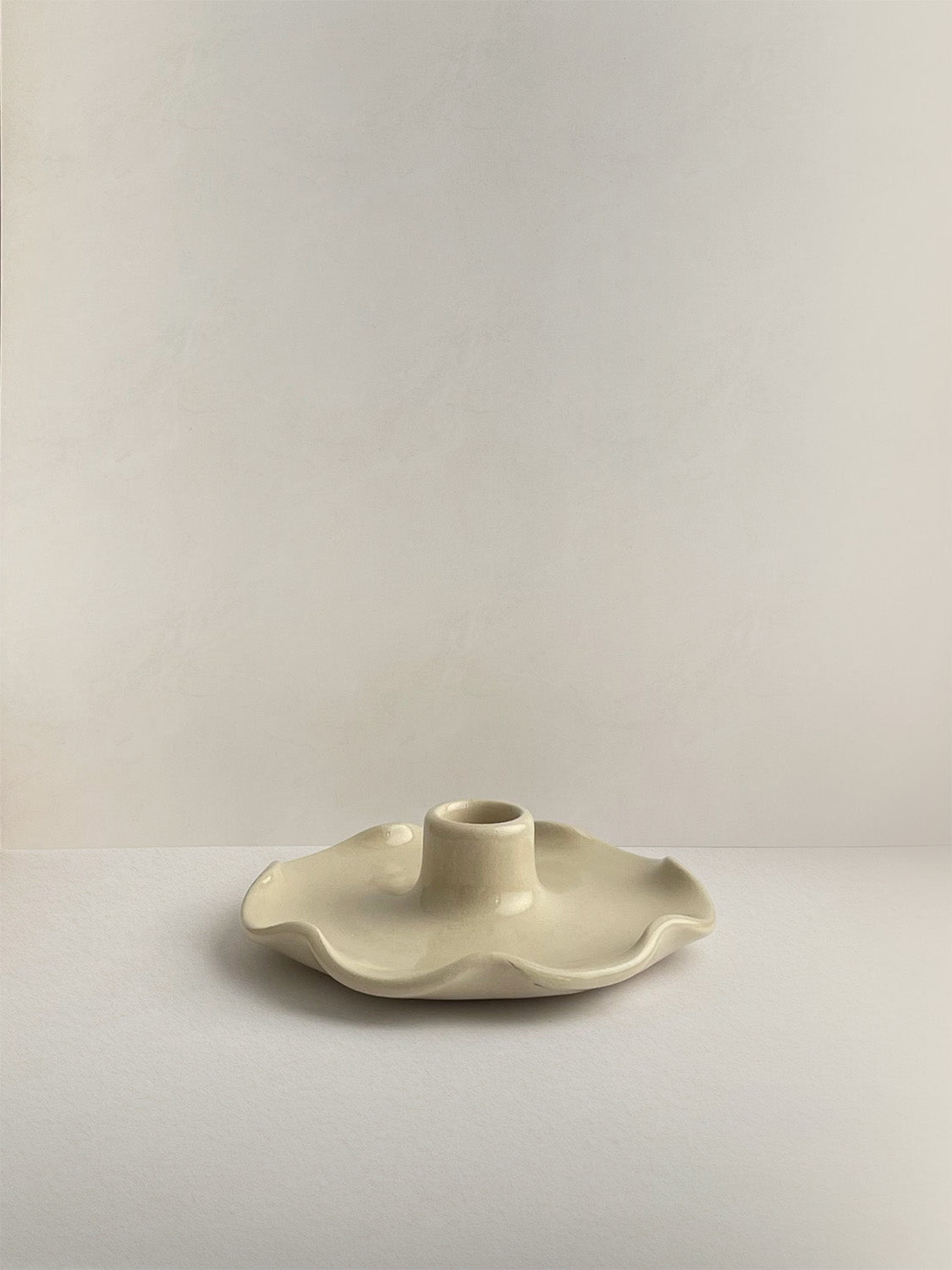 A handmade ceramic candle holder with a softly frilled base and a central cylindrical stem, on a neutral background.