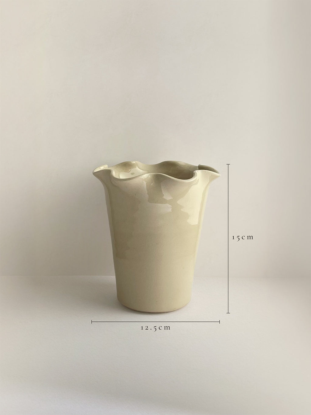 A handmade ceramic cream coloured vase with a frilled, wavy rim and dimensions shown, on a neutral background.