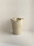 A handmade ceramic cream coloured vase with a frilled, wavy rim on a neutral background.
