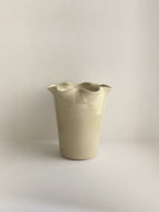 A handmade ceramic cream coloured vase with a frilled, wavy rim on a neutral background.