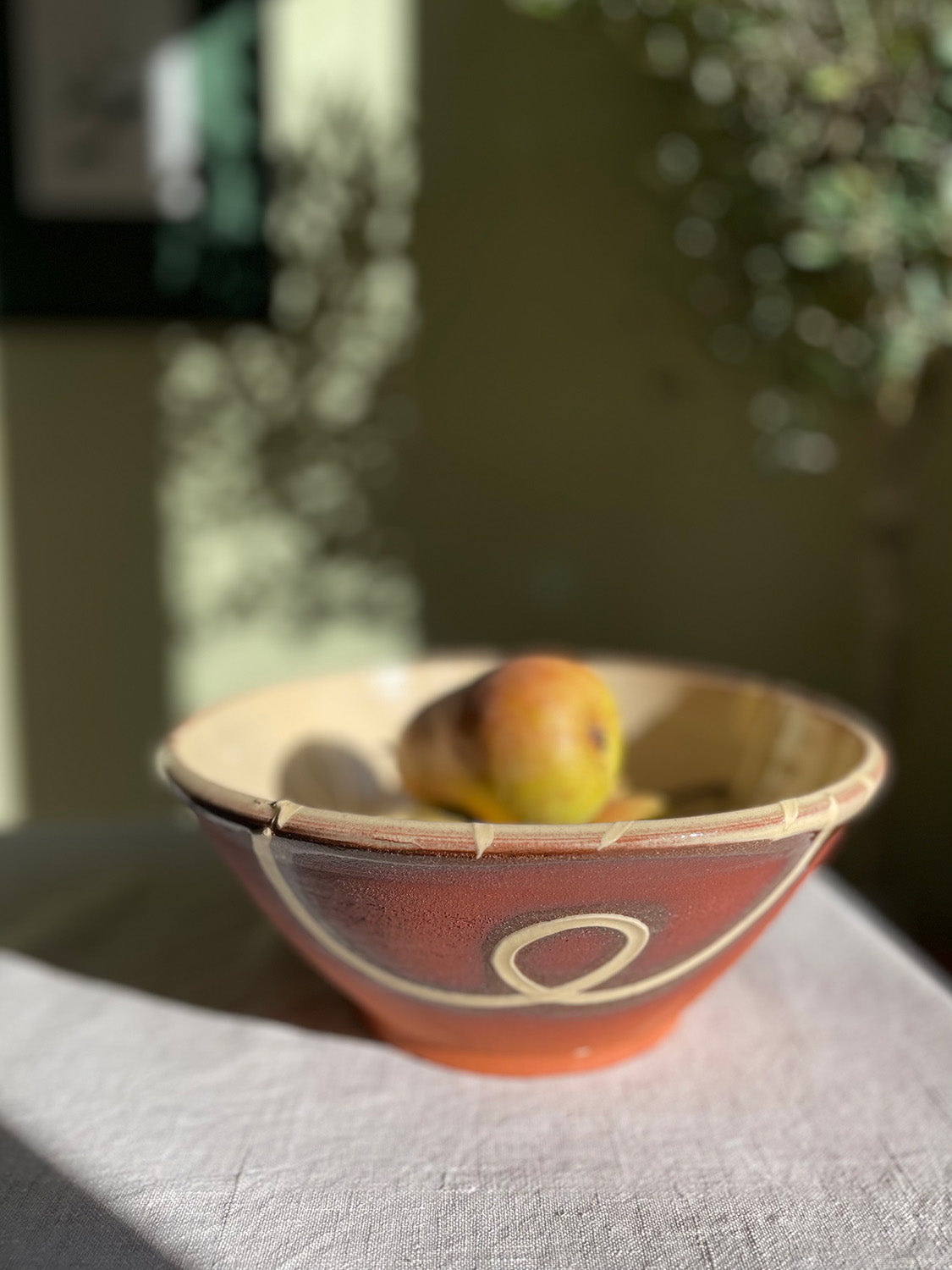 Ceramic serving bowl with pears on a linen tablecloth with blurred greenery in the background.