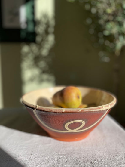 Ceramic serving bowl with pears on a linen tablecloth with blurred greenery in the background.