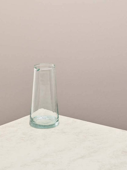 Clear glass jug on a light surface with a beige background.