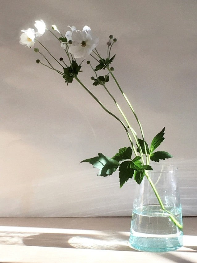 Handmade recycled glass tapered vase with white flowers on a neutral background.