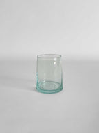 A handmade clear tumbler made from recycled glass with a light aqua tint, on a light neutral background.