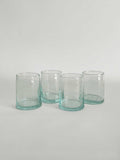 Set of four handmade clear tumblers made from recycled glass with a light aqua tint, arranged in a row on a light neutral background.