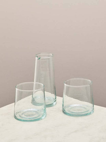 Two clear glasses and a small jug on a light surface against a beige background.