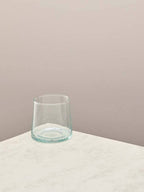 Clear glass low tumbler on a light surface with a beige background.