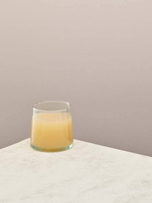 A single clear handmade recycled low tumbler with a drink on a light surface.