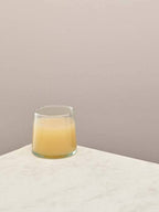 A single clear handmade recycled low tumbler with a drink on a light surface.
