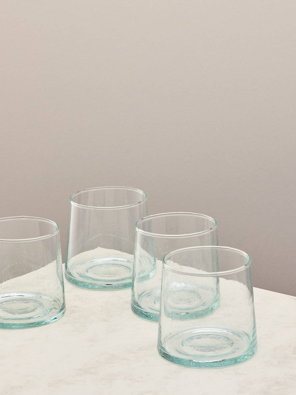 A set of four clear handmade recycled low tumblers on a light surface.
