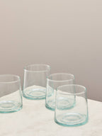 A set of four clear handmade recycled low tumblers on a light surface.