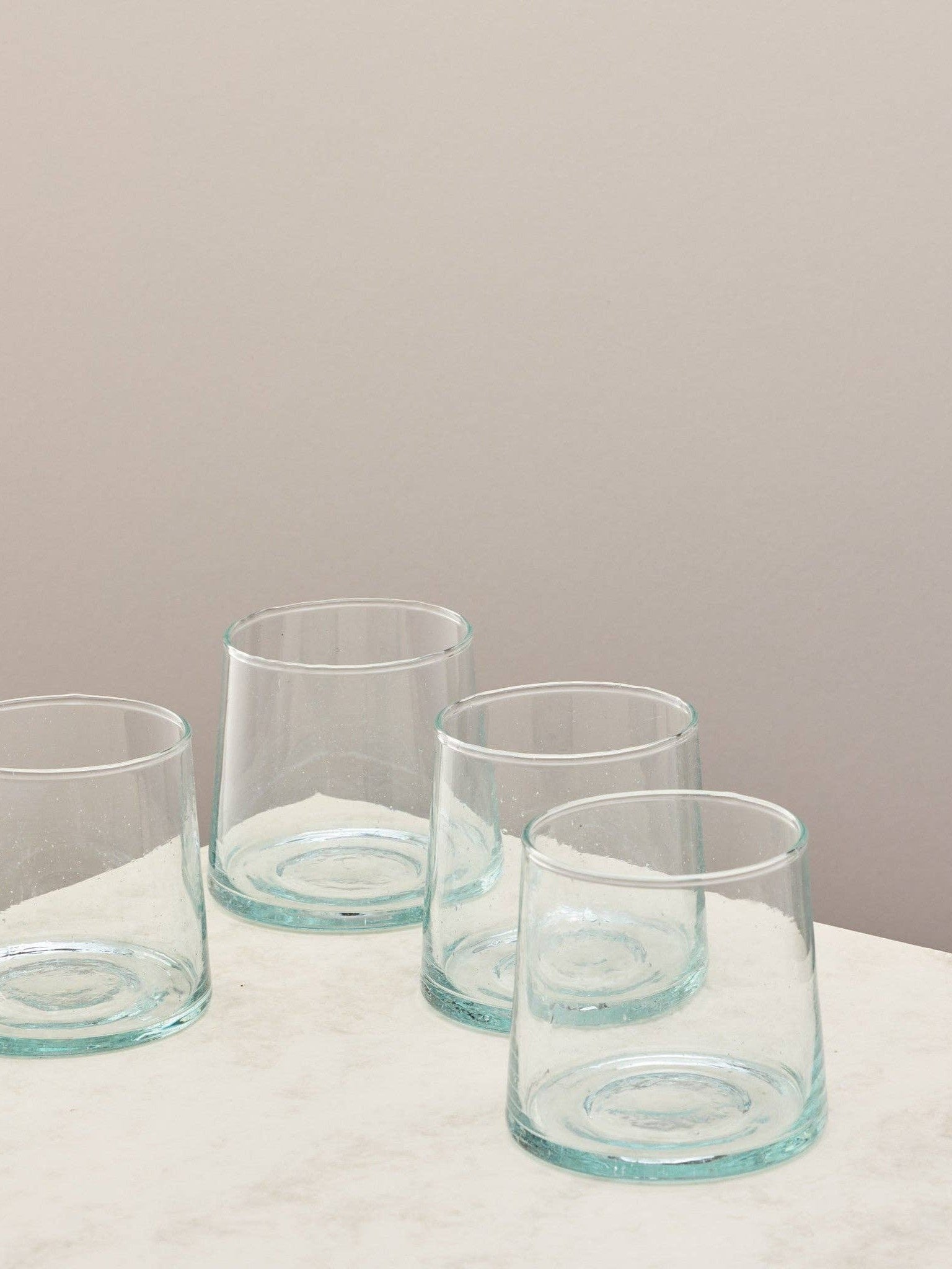 A set of four clear handmade recycled low tumblers on a light surface.