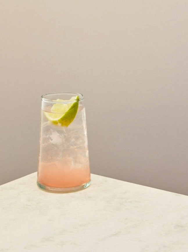 Handmade recycled tall glass with cocktail on a light surface.