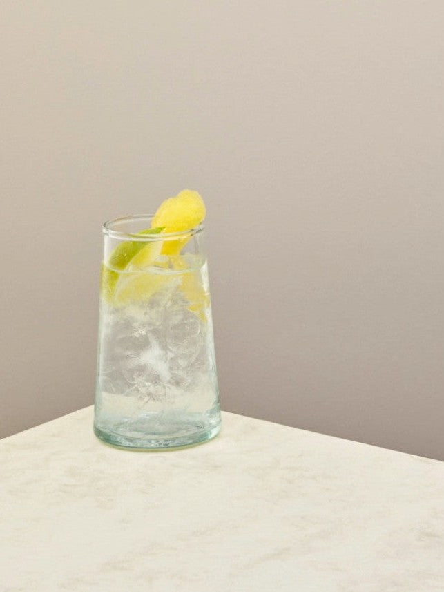 Handmade recycled tall glass with iced water and lemon on a light surface.
