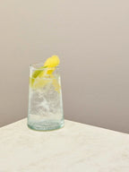 Handmade recycled tall glass with iced water and lemon on a light surface.