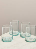 A set of four clear handmade recycled tumblers on a light surface.