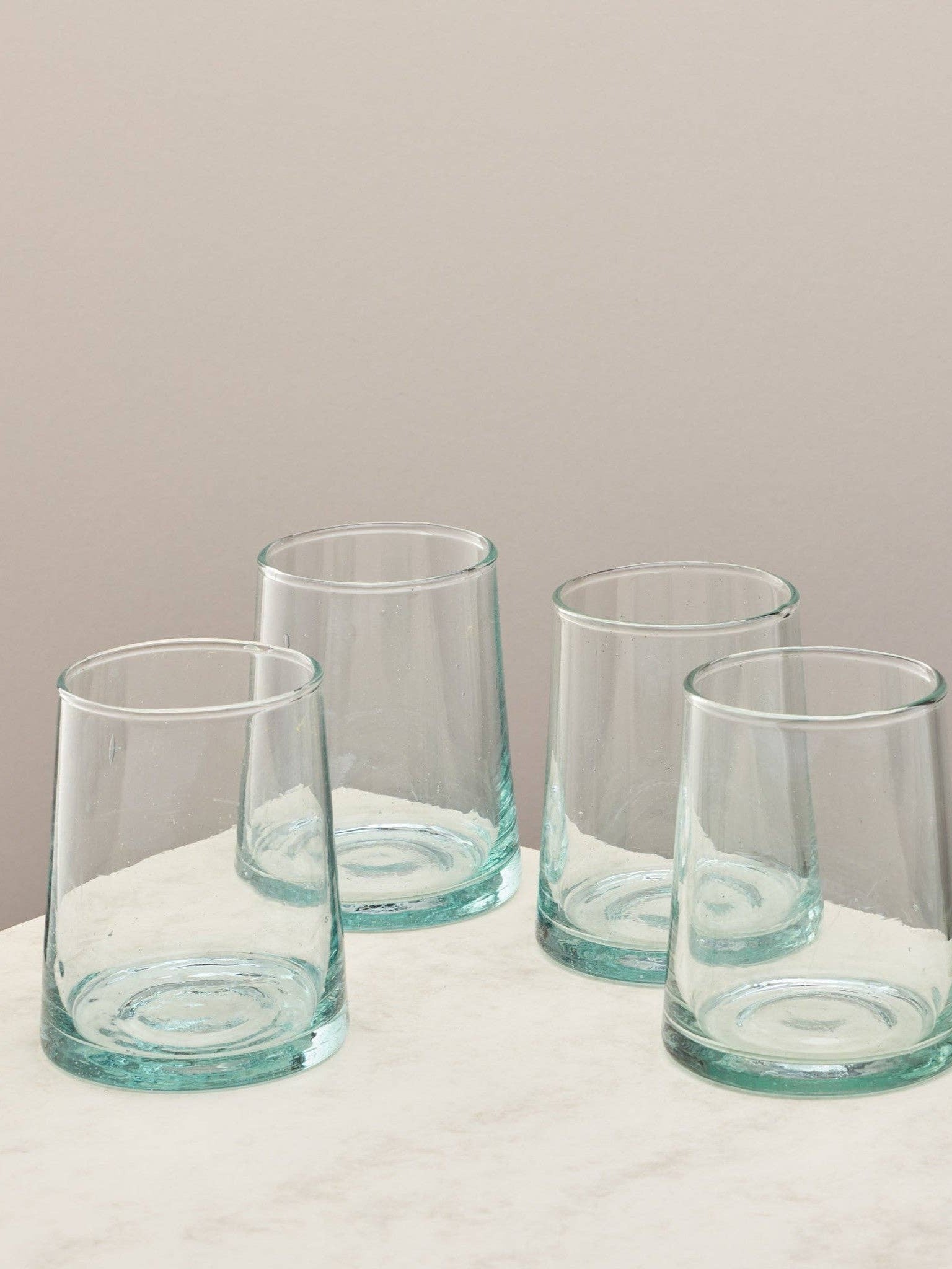 A set of four clear handmade recycled tumblers on a light surface.