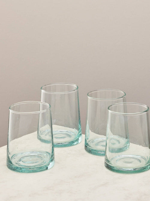 A set of four clear handmade recycled tumblers on a light surface.