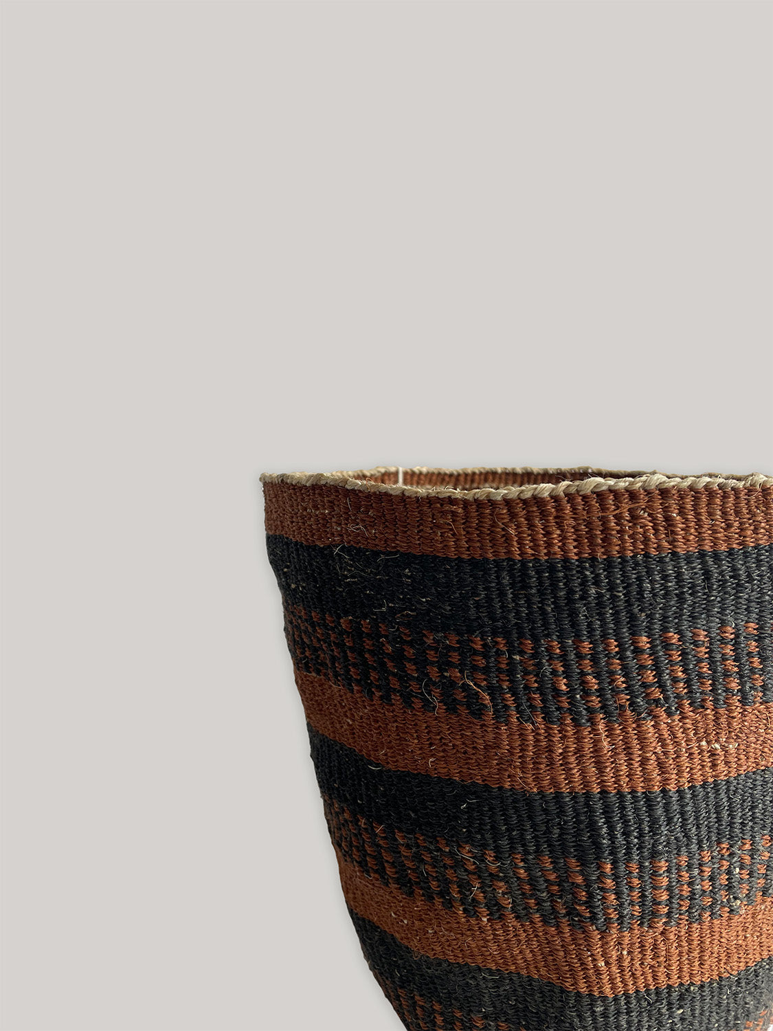Close-up detail of woven basket with rust brown and black stripes on a neutral background.