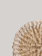 Close-up of round handwoven sisal coaster on a neutral background.