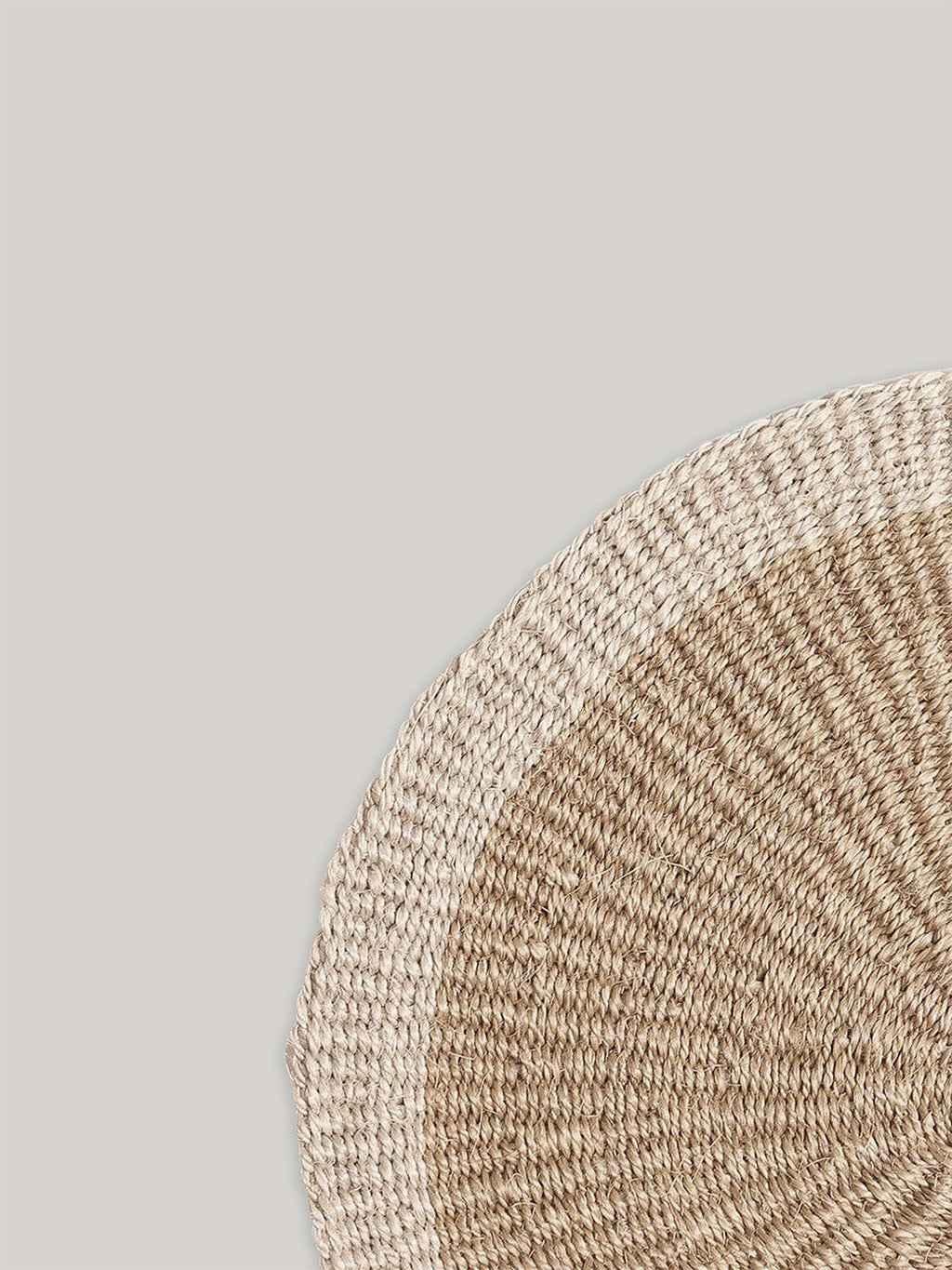 Close-up of round handwoven sisal placemat on a neutral background.