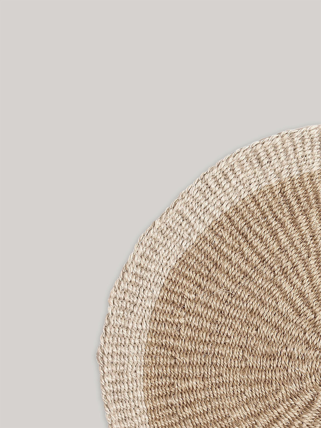 Close-up of round handwoven sisal placemat on a neutral background.