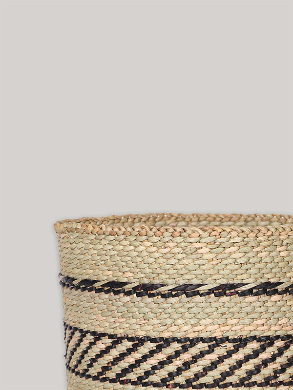 Handwoven storage basket in black and natural pattern on plain taupe background - corner detail.