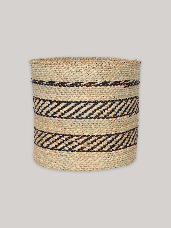 Handwoven storage basket in black and natural pattern on plain taupe background - front.