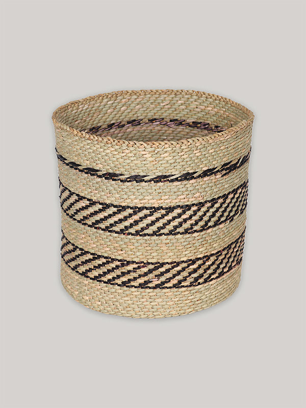 Handwoven storage basket in black and natural pattern on plain taupe background - front.