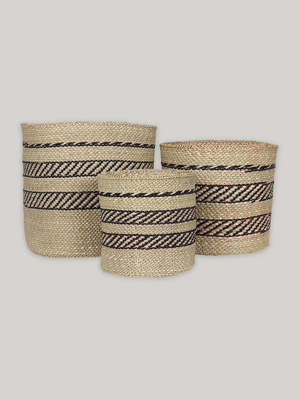 Group of three handwoven storage baskets in black and natural pattern on plain taupe background - front.