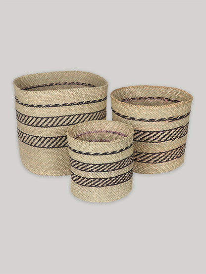 Group of three handwoven storage baskets in black and natural pattern on plain taupe background - front.