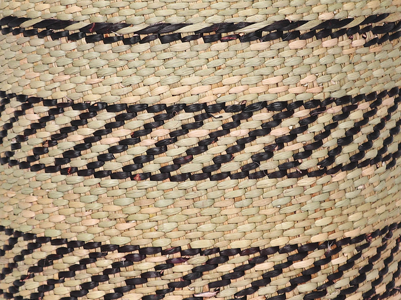 Handwoven storage basket in black and natural pattern on plain taupe background - weave detail.