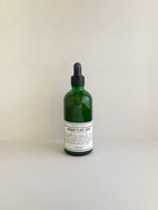 Indoor plant food solution in a dark green glass dropper bottle with a black cap and a white label, on a neutral background.