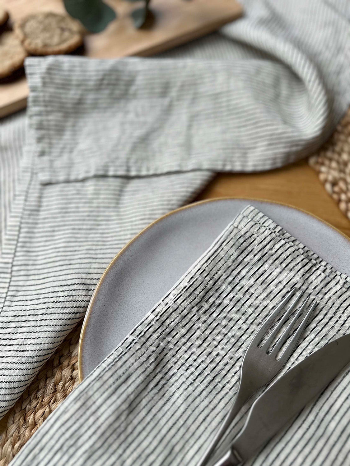100% linen napkin set in black and ivory stripe, on a table setting with white plate, silver cutlery and woven placemats.