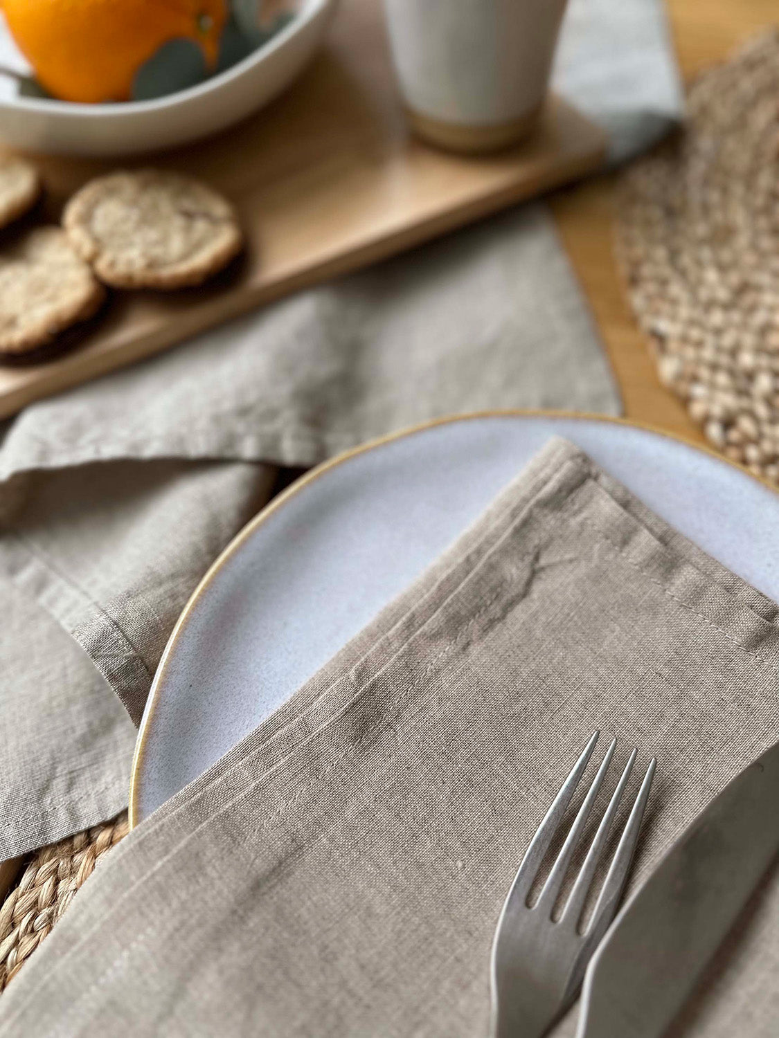 100% linen napkin set in natural colour, on a table setting with white plate, silver cutlery and woven placemats.