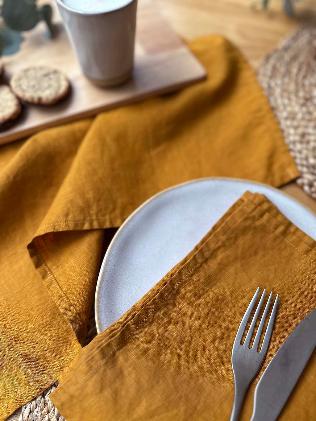 100% linen napkin set in spice colour, on a table setting with white plate, silver cutlery and woven placemats.