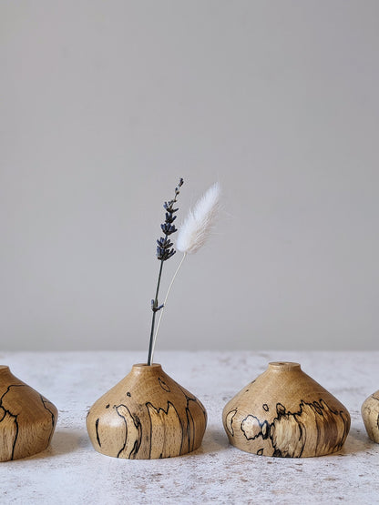 Group of low miniature bud vases in spalted Beech with dried stems, on a mottled off-white surface against a plain taupe wall - front view.