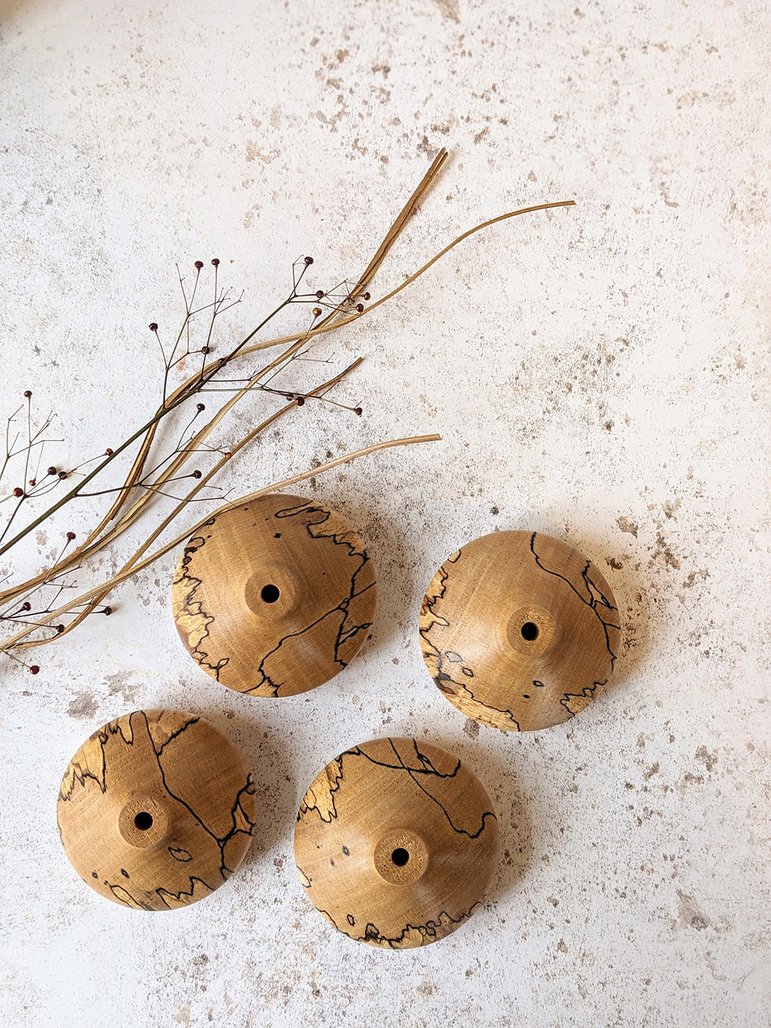 Group of low miniature bud vases in spalted Beech with dried stems, on a mottled off-white surface - top view.