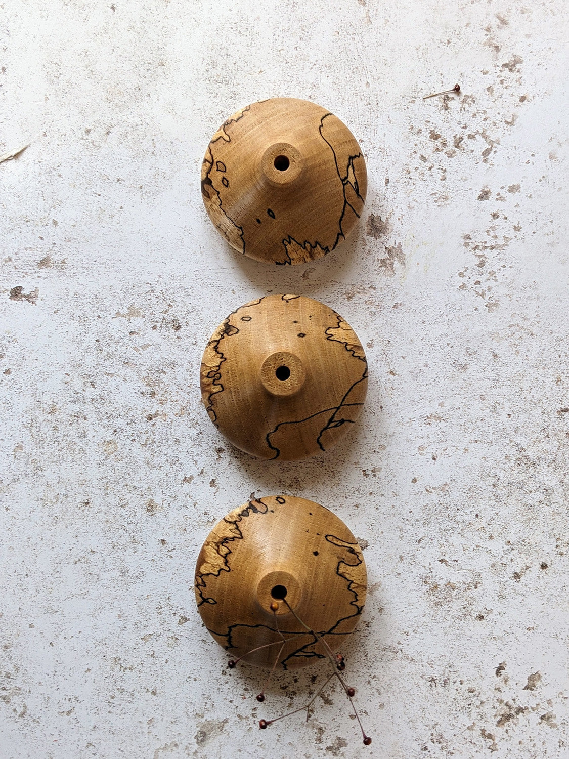 Group of three low miniature bud vases in spalted Beech, on a mottled off-white surface - top view.