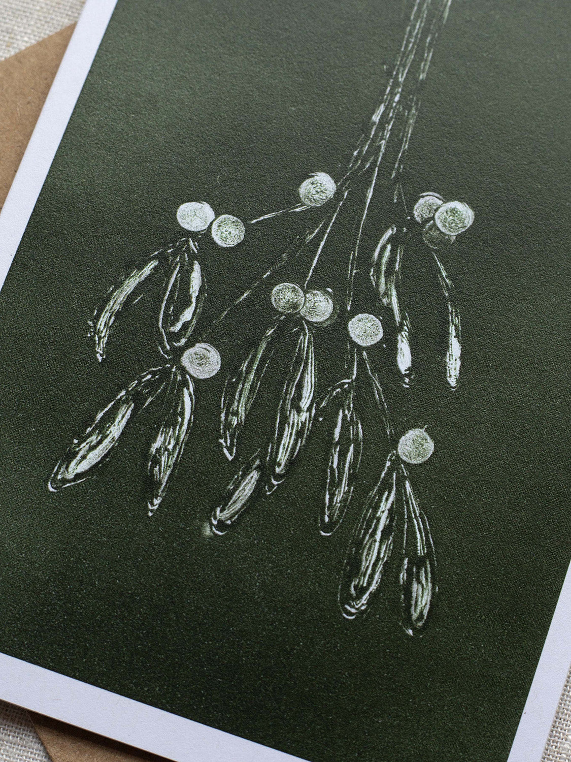 Close-up of botanical Christmas card with mistletoe design on a dark green background.