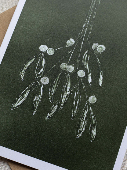 Close-up of botanical Christmas card with mistletoe design on a dark green background.