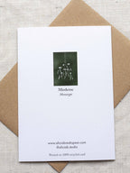 Reverse side of botanical Christmas card with mistletoe design on a dark green background, placed on a linen surface with a Kraft paper envelope.