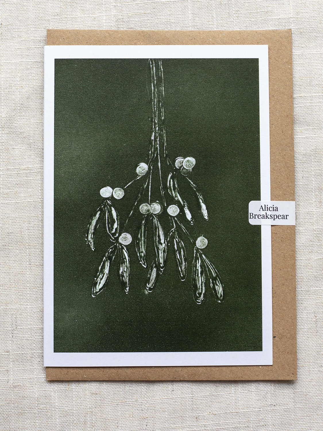 Botanical Christmas card with mistletoe design on a dark green background, with a Kraft paper envelope and 'Alicia Breakspear' sticker seal.