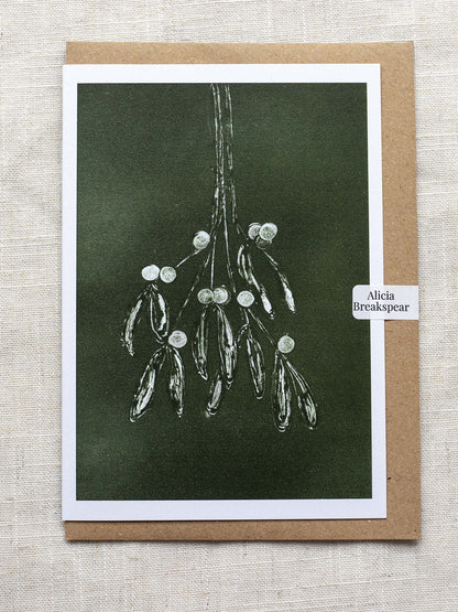 Botanical Christmas card with mistletoe design on a dark green background, with a Kraft paper envelope and 'Alicia Breakspear' sticker seal.